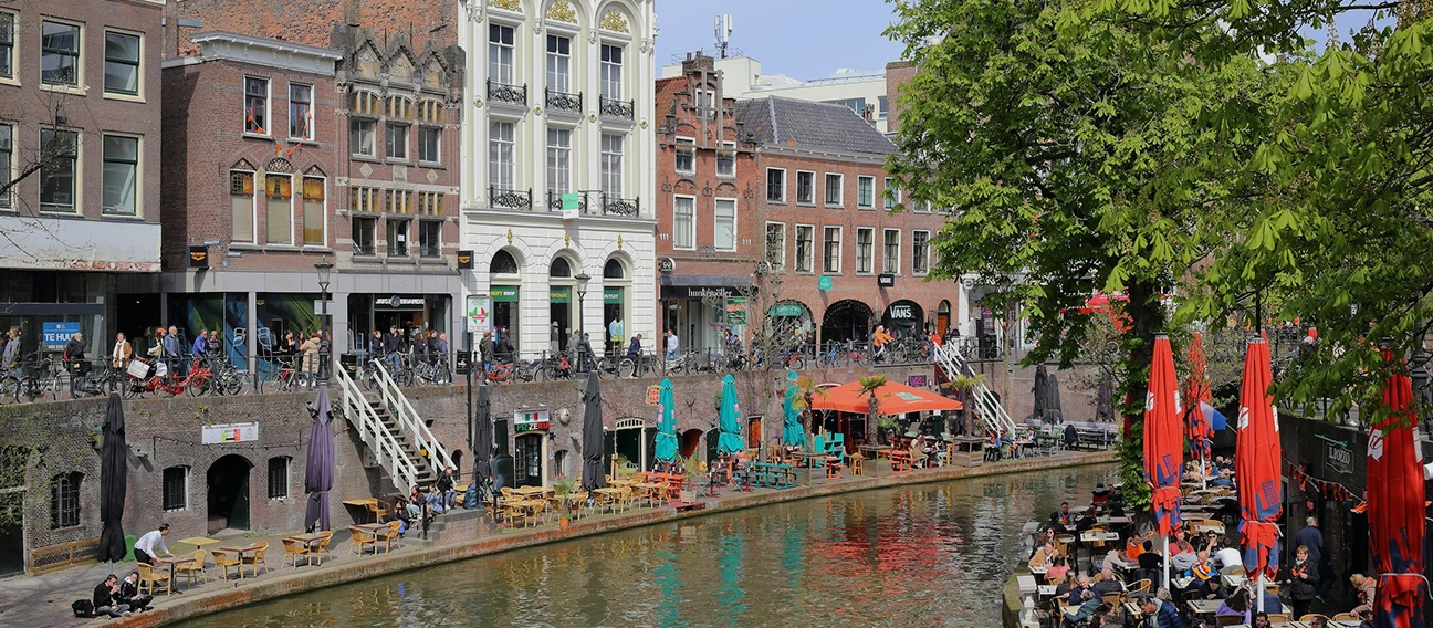 Foto van een gracht in Utrecht waarbij mensen op het terras zitten.
